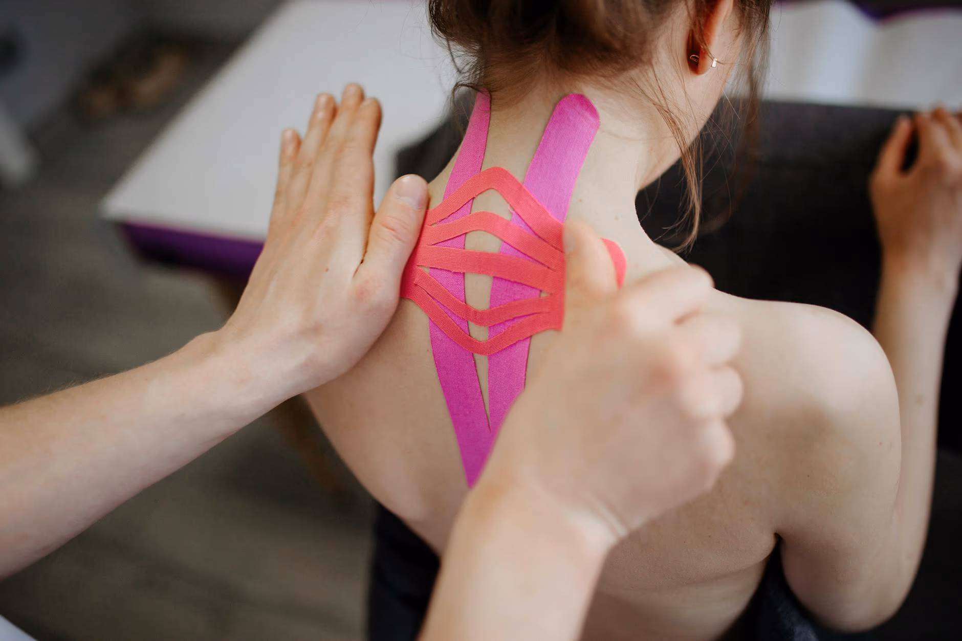 Physiotherapeutin klebt Kinesio-Tape auf Schulter eines Sportlers